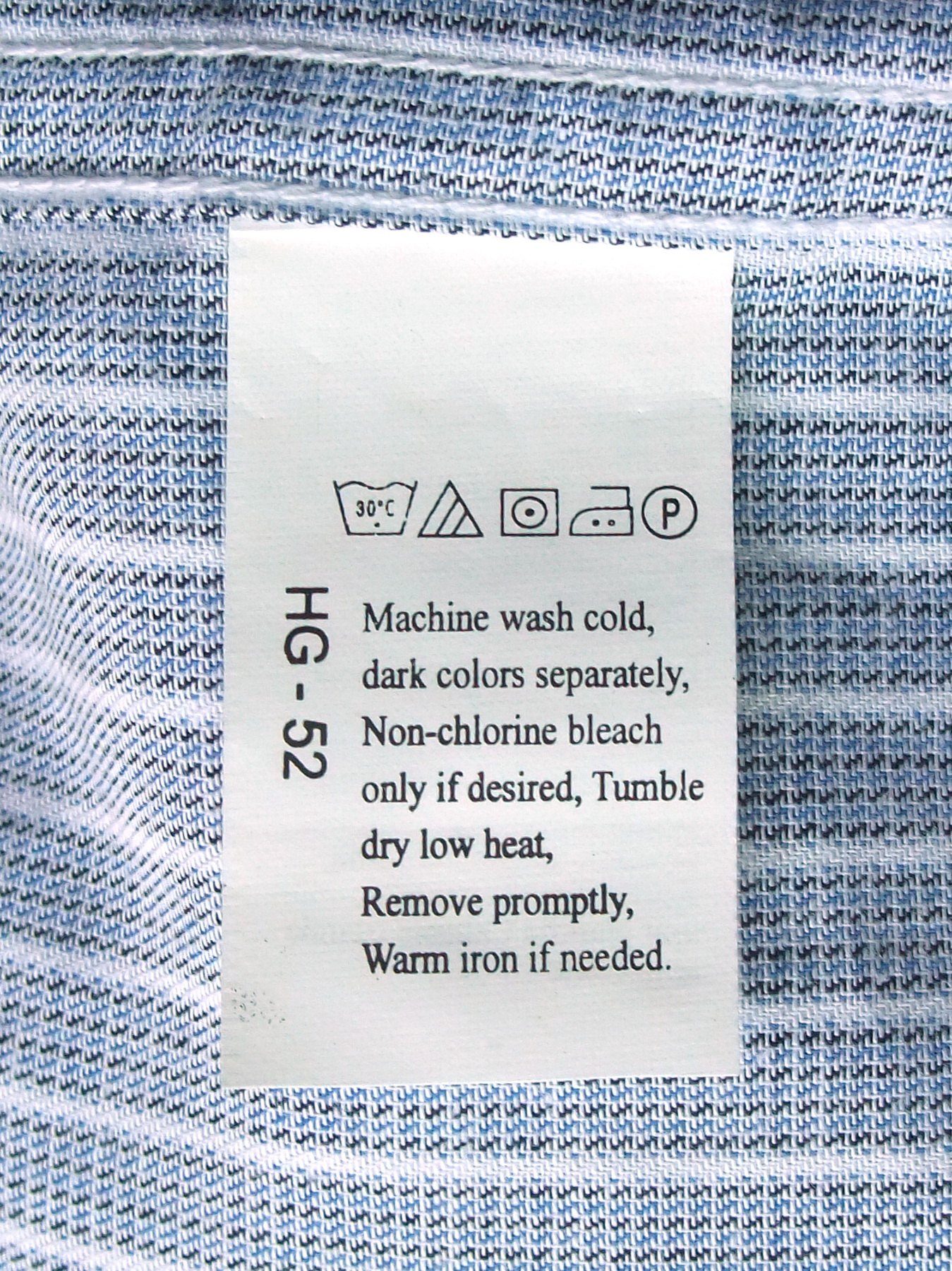 Etiqueta de cuidado blanca cosida en una camisa de rayas azules, con símbolos de lavado y texto de instrucciones