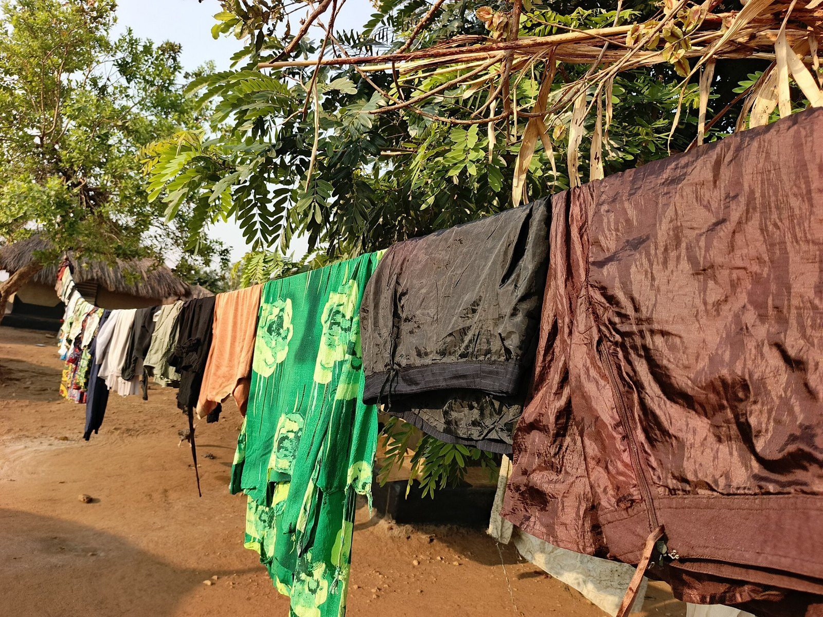 Ropa de varios colores colgada de una cuerda de alambre al aire libre, entre árboles y con el suelo de tierra al fondo