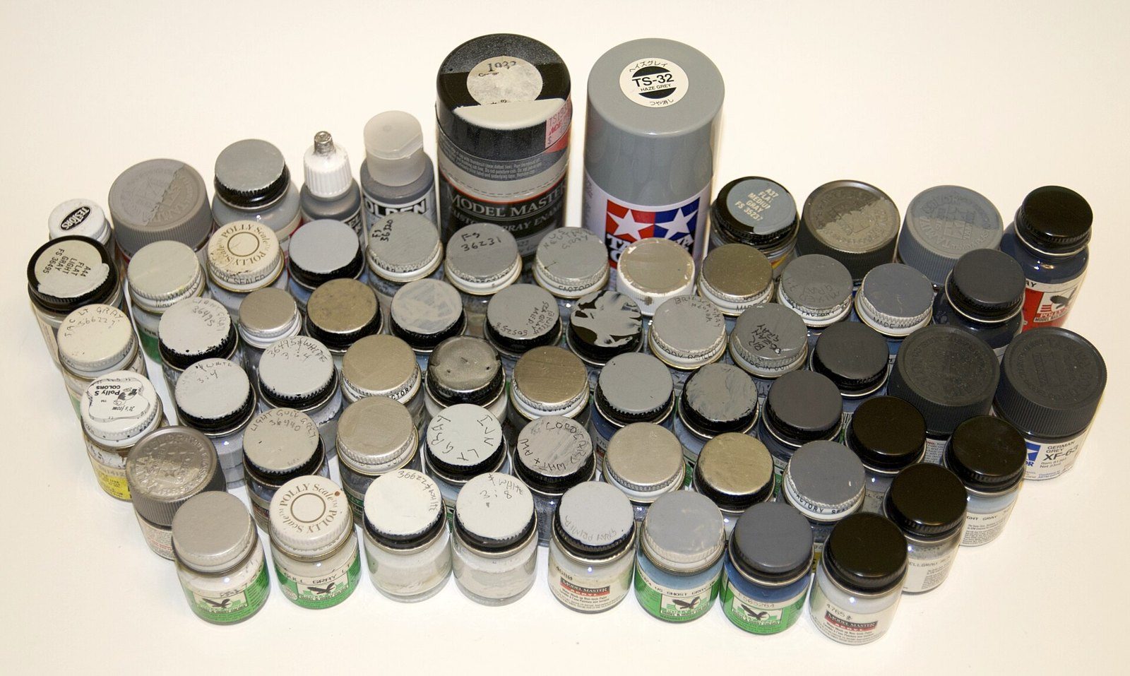 Decenas de frascos de pintura acrílica al agua en distintos tonos de gris, dispuestos sobre una mesa blanca