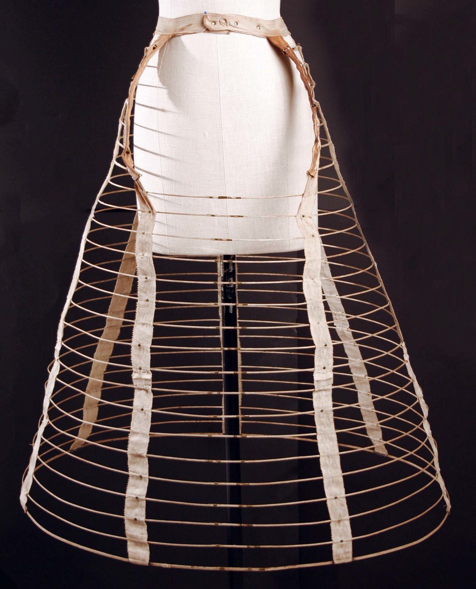 Crinolina de jaula de aros de acero unidos por cintas de tela, vista de frente sobre un maniquí